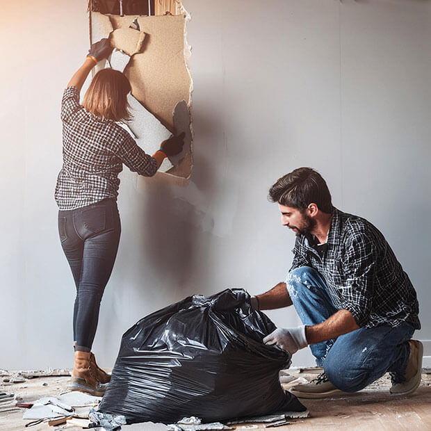 Two people removing drywall and placing it in a trash bag